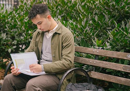 young male student sitting on a bench reading a textbook